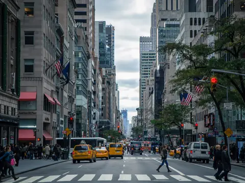 A Manhattan avenue with yellow cabs, people crossing and tall buildings