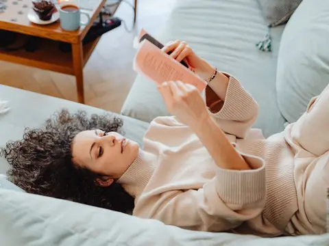 A woman in a cream sweater reading on a sofa in soft daylight